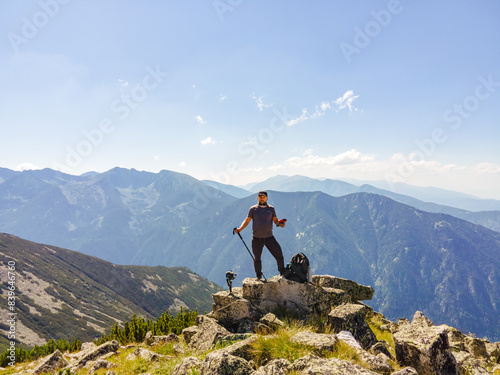 Young man takes selfie with drone while standing on top of large mountain on sunny day in summer. Aerial view mountain ranges surface blue sky of mountain, Bulgaria, Borovets, Musala peak. Hiking