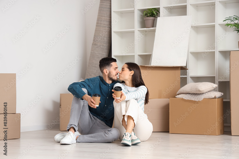 Young couple with coffee cups kissing in room on moving day Young couple with coffee cups kissing in room on moving day