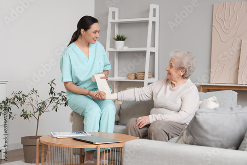 Senior woman with physical therapist bandaging her arm at home