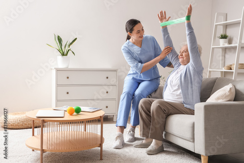 Senior woman with stretching band and physical therapist at home photo