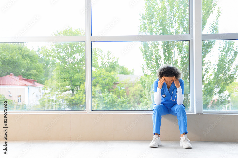 Stressed mature female doctor sitting on windowsill in clinic Stressed mature female doctor sitting on windowsill in clinic