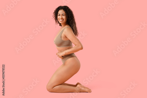 Beautiful young happy African-American woman in stylish underwear sitting on pink background