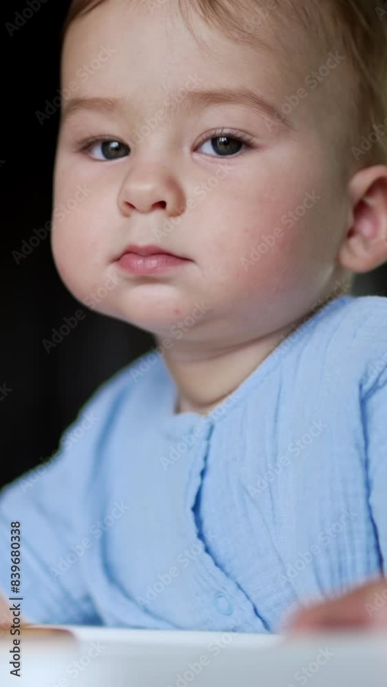 Serious thoughtful baby boy sitting at the table. Kid playing with food, throwing bagel on the floor and looking at it. Close up. Vertical video Serious thoughtful baby boy sitting at the table. Kid playing with food, throwing bagel on the floor and looking at it. Close up. Vertical video