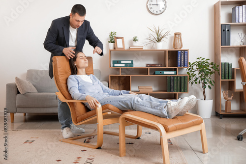 Male psychologist with pendulum hypnotizing young woman in office