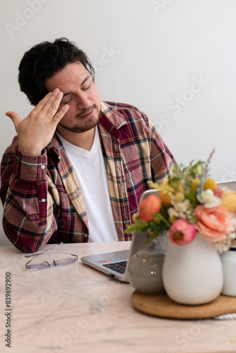 Young man with headache with his laptop in the living room making pain gesture