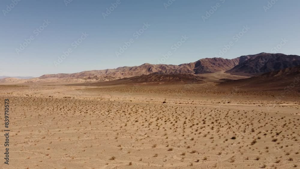 Drone Panoramic Shot from Above of an Orange Desert with Dry Terrain, Majestic Mountains, Blue Sky, and Expansive Empty Land Drone Panoramic Shot from Above of an Orange Desert with Dry Terrain, Majestic Mountains, Blue Sky, and Expansive Empty Land