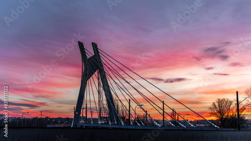 Aerial panoramic view of sunset cityscape with suspension bridge silhouette in Krakow, Poland. Drone photo of modern bridge with steel cables and concrete tower in purple, red and blue sky clouds photo