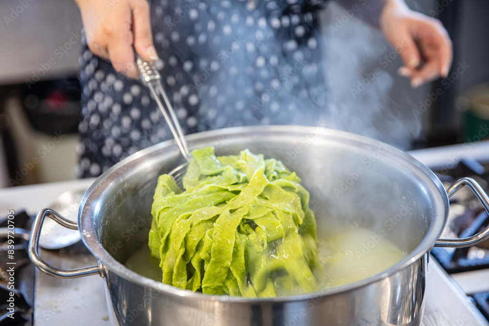 Spinach Green Pasta. Spinach pasta. Female chef throws green spinach pasta dough into a boiling pot on the stove, cooking pasta. Spinach Green Pasta. Spinach pasta. Female chef throws green spinach pasta dough into a boiling pot on the stove, cooking pasta.