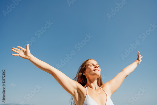 A woman is standing in the sun with her arms outstretched, looking up at the sky