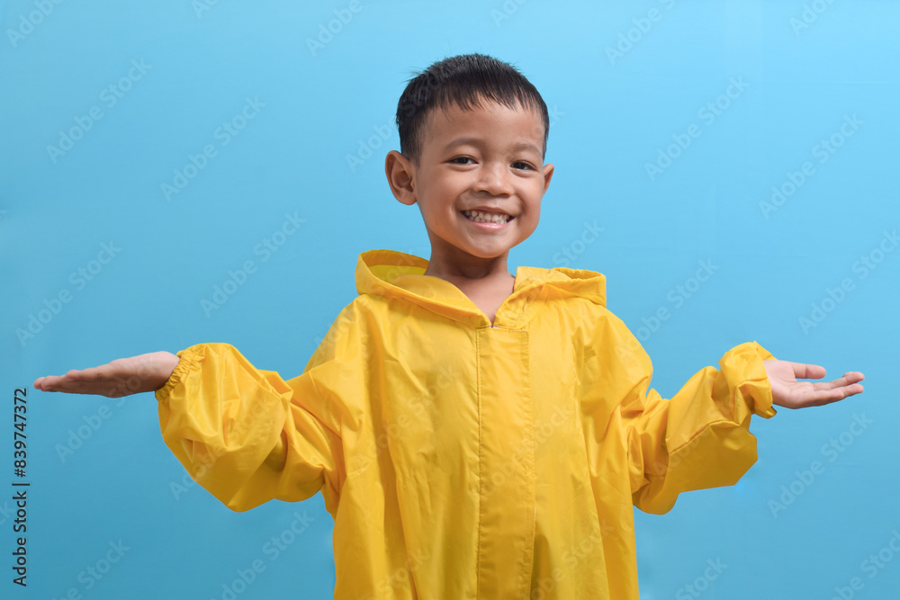 Cute little Asian boy wearing a yellow raincoat isolated on blue background. Weather forecast concept Cute little Asian boy wearing a yellow raincoat isolated on blue background. Weather forecast concept