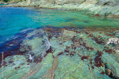 A rocky cliff with a moss-covered surface overlooks a vast blue ocean.