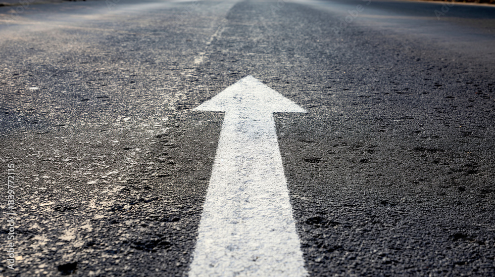 An asphalt road stretches into the distance with a painted white arrow ...
