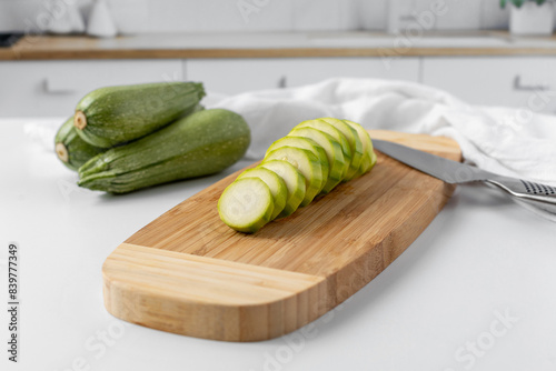 One Zucchini Sliced on a Cutting Board with Three Whole Zucchini in the Background of a Kitchen
