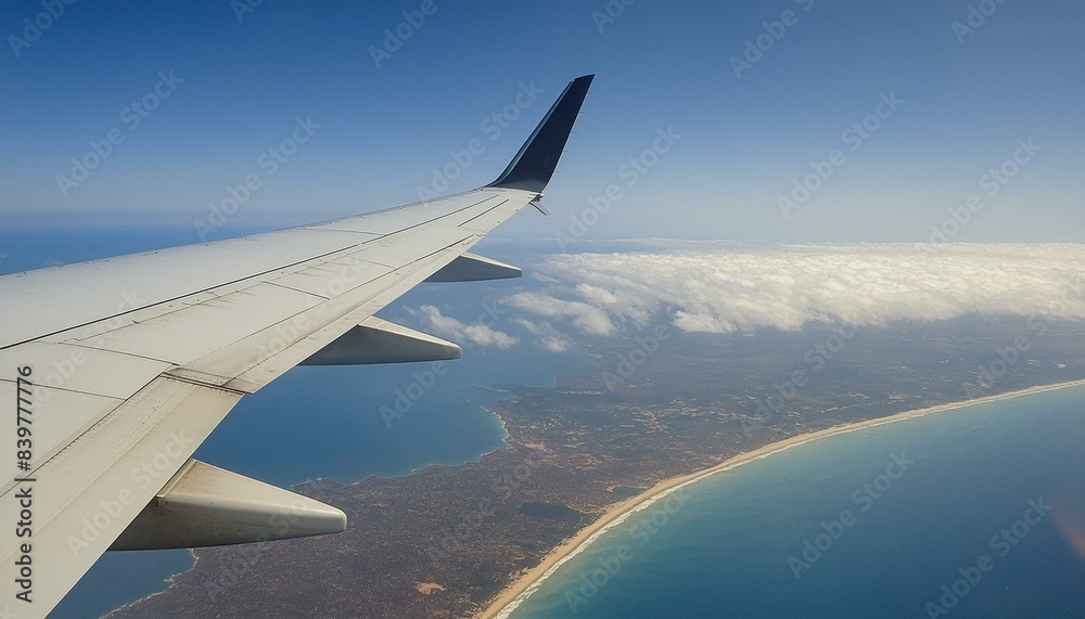 Airplane wing view from window. Clouds, beach, and ocean below. Conveys a sense of altitude and travel Airplane wing view from window. Clouds, beach, and ocean below. Conveys a sense of altitude and travel