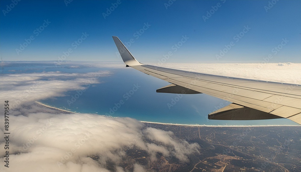 Fototapeta premium Airplane wing view from window. Clouds, beach, and ocean below. Conveys a sense of altitude and travel