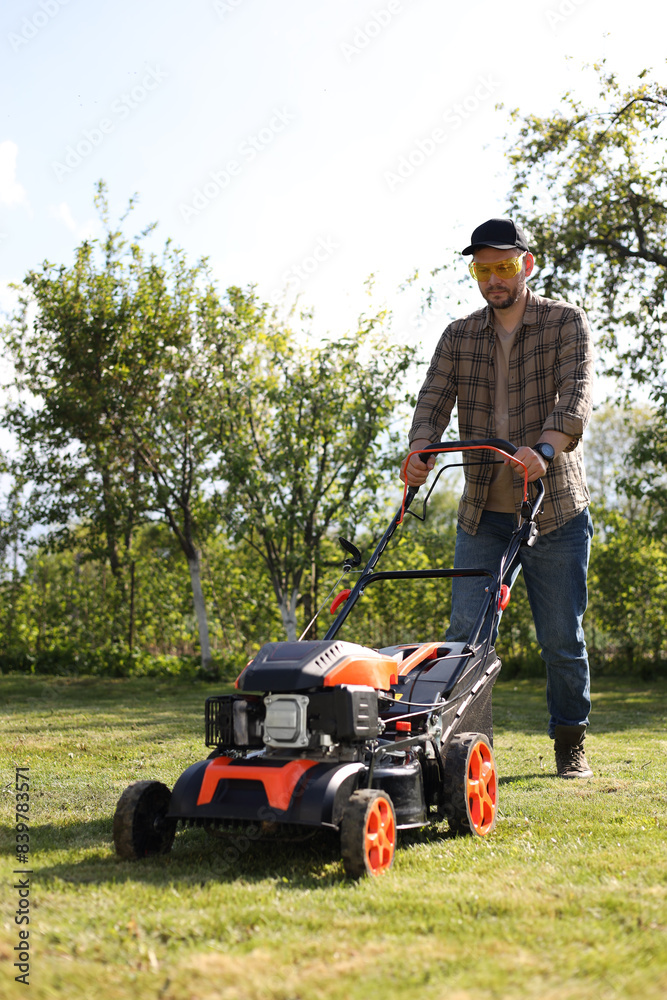 Fototapeta premium Man cutting green grass with lawn mower in garden