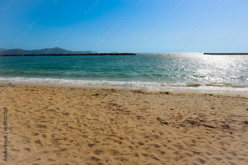 a deserted sandy beach with calm, blue water and blue sky in the background. a deserted sandy beach with calm, blue water and blue sky in the background.