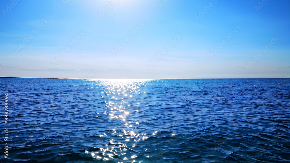 Fototapeta premium A single wave crests on a serene ocean, with a clear azure sky and sunlight casting glittering reflections on the water.