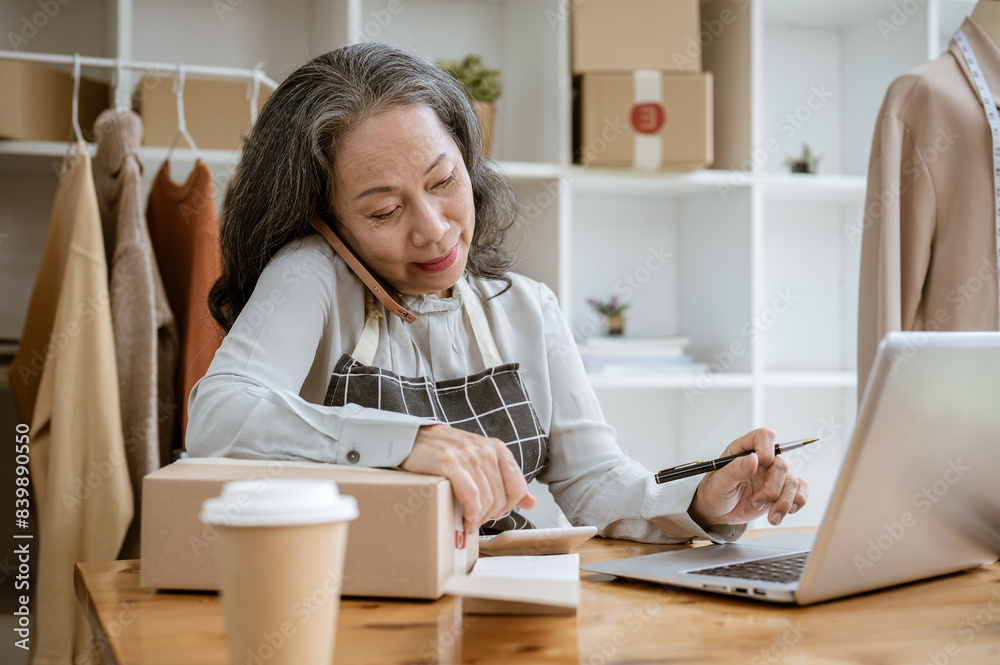 A focused female online clothes seller is talking on the phone while working in her studio. A focused female online clothes seller is talking on the phone while working in her studio.