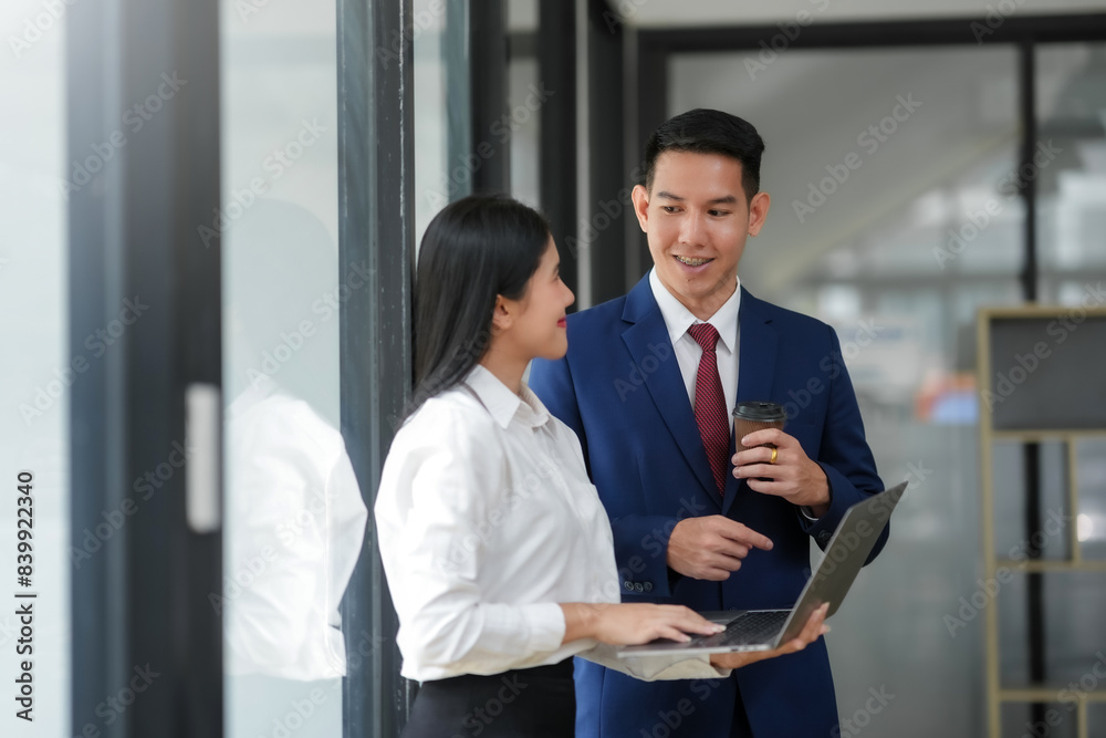 Business professionals discussing work in modern office setting, woman with laptop and man holding coffee, wearing formal attire. Business professionals discussing work in modern office setting, woman with laptop and man holding coffee, wearing formal attire.