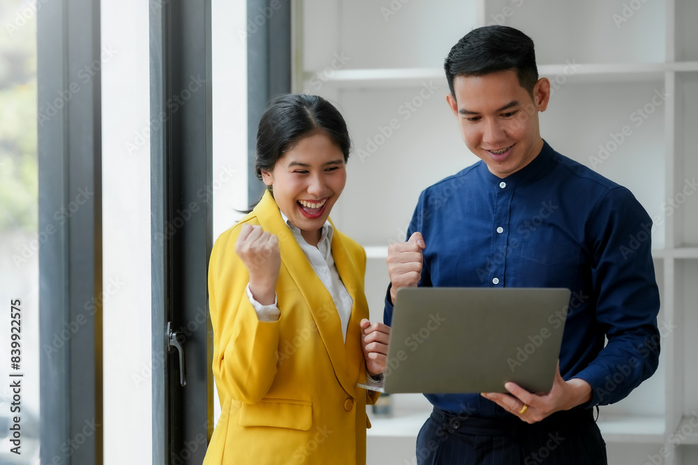 Excited business colleagues celebrating success while looking at a laptop screen in a modern office environment. Excited business colleagues celebrating success while looking at a laptop screen in a modern office environment.