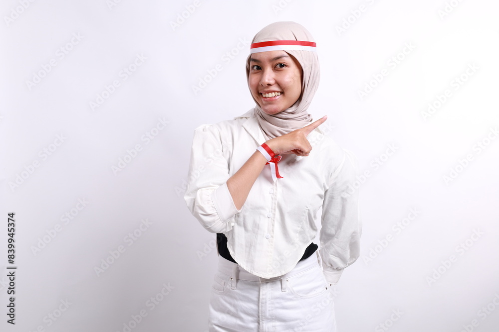 A happy Asian muslim woman wearing white hijab and red white flag ribbon, and pointing copy space on top of her, isolated by white background. Indonesia's independence day A happy Asian muslim woman wearing white hijab and red white flag ribbon, and pointing copy space on top of her, isolated by white background. Indonesia's independence day