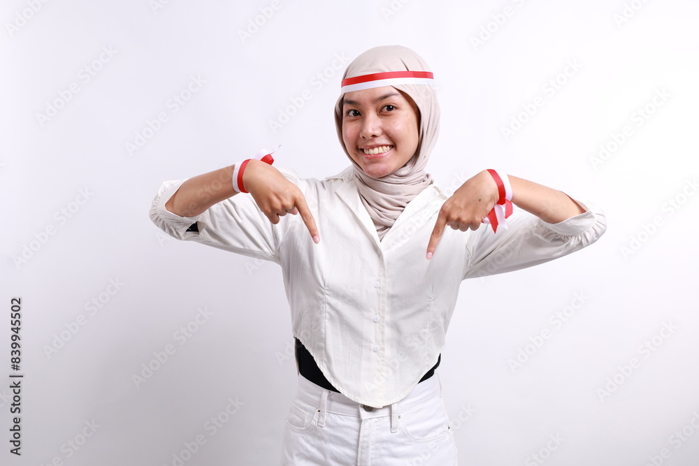 Happy Asian muslim woman wearing Indonesia flag colored headband smiling cheerfully and pointing down at the copy space. Independence day advertisement concept Happy Asian muslim woman wearing Indonesia flag colored headband smiling cheerfully and pointing down at the copy space. Independence day advertisement concept