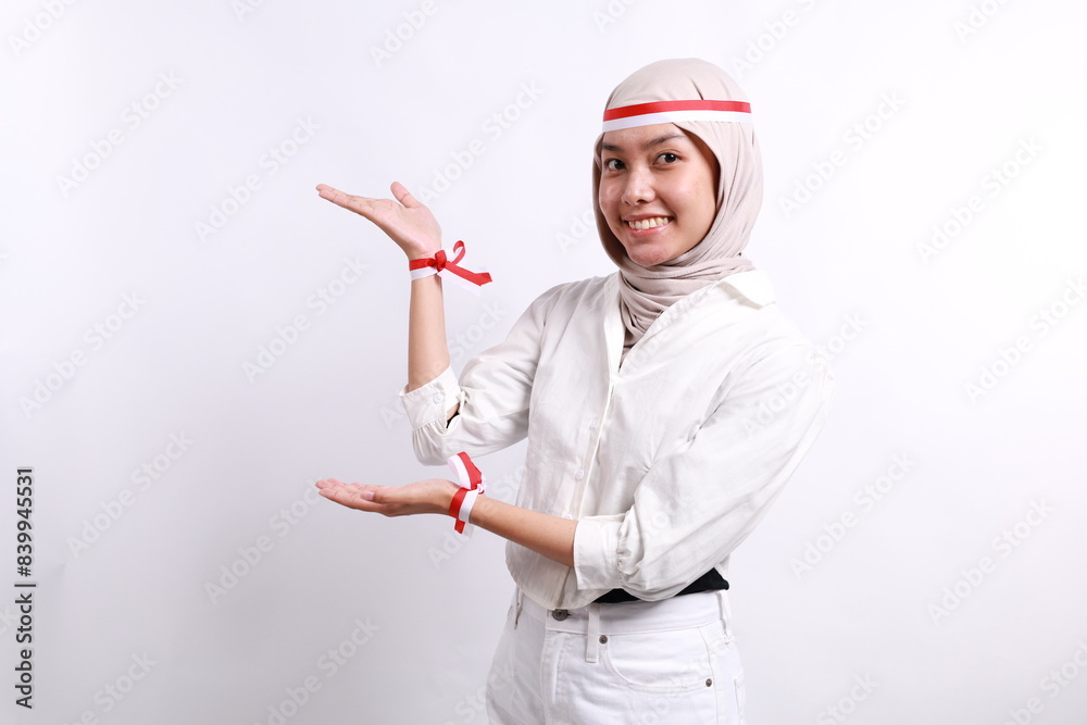 Excited Asian muslim woman wearing red white flag headband presenting at the copy space on the side. Independence day advertisement concept Excited Asian muslim woman wearing red white flag headband presenting at the copy space on the side. Independence day advertisement concept