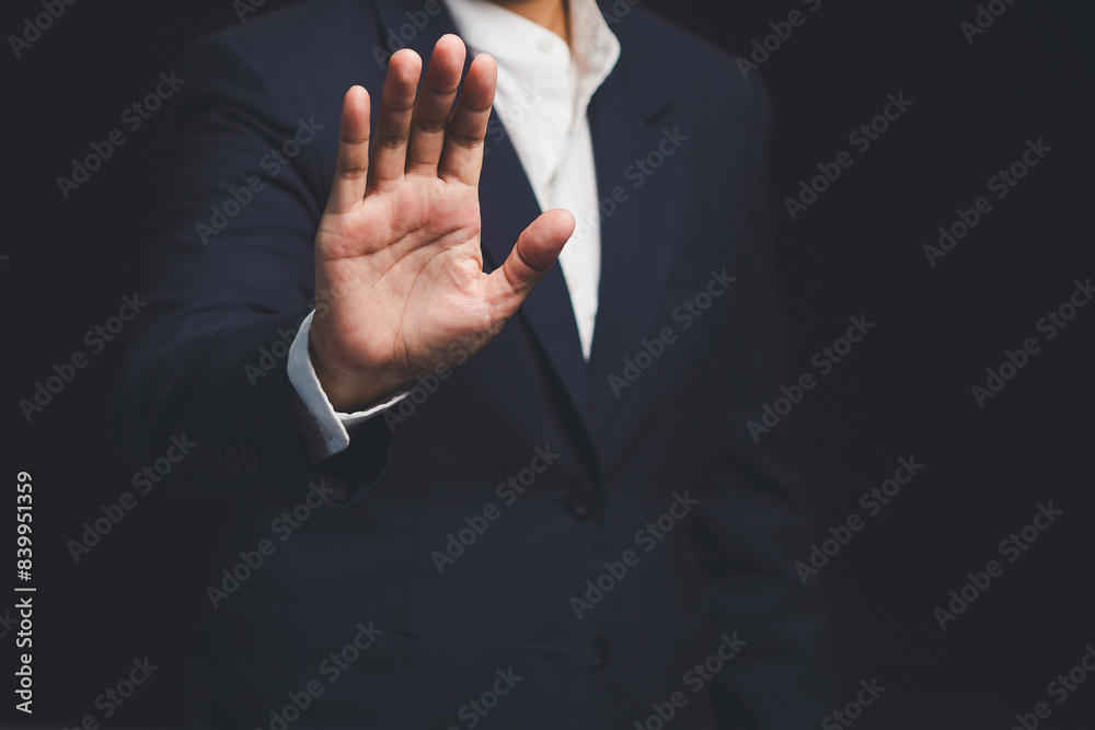 Fototapeta premium Businessman shows a stop gesture while standing on a black background.