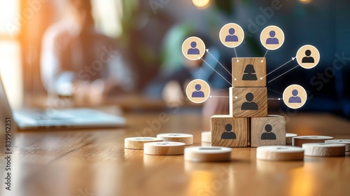 Wooden blocks with human icons stacked, representing a network of people.  A blurred laptop and coins in the background.  Concept for teamwork, connection, and community.