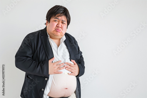 Obese Japanese man in his thirties frowning and clutching his belly flab against a white background