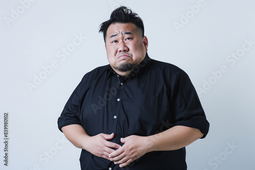 Obese Japanese woman in her thirties frowning and clutching her belly flab against a white background
