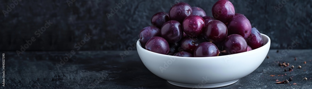 Deep purple jamun fruits in a white ceramic bowl, with one fruit opened to show the juicy, dark interior, set against a dark background Deep purple jamun fruits in a white ceramic bowl, with one fruit opened to show the juicy, dark interior, set against a dark background