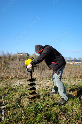 The man drills the ground with handy rig machine. Drilling the hole in land. Boring for the fence installation. Bore tool. Handy equipment. Portable manual earth auger for planting trees. Copy space