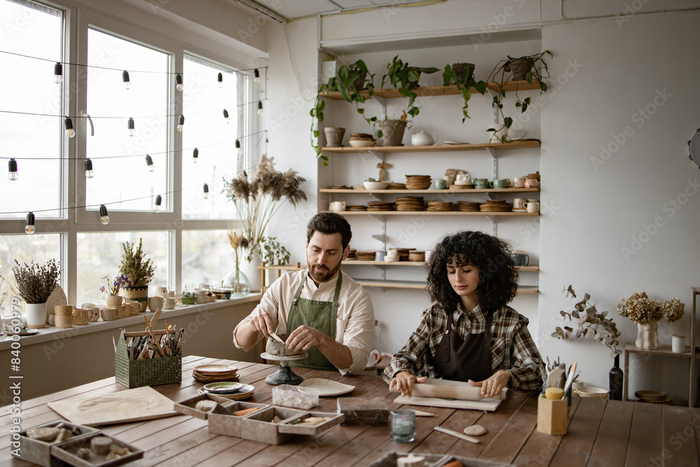 Bearded mature man and woman creating pottery pieces in well-lit studio ...