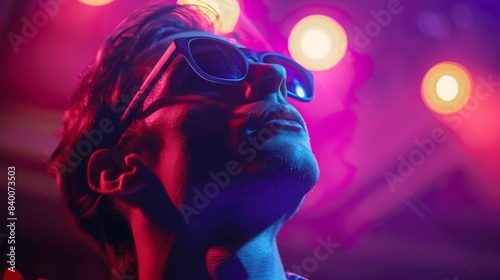 An attractive young man wearing sunglasses in a nightclub with a purple and pink spotlight.