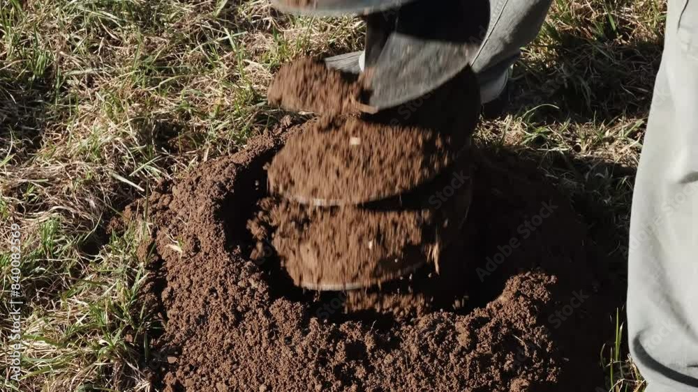 Drilling the ground with rig machine. The man drills the hole in land. Borering for the fence installation. Bore tool. Handy equipment. Portable manual earth auger for planting bushes and trees. 4K