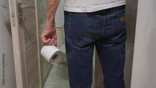 An older man's hand holding a roll of toilet paper in front of the toilet.
