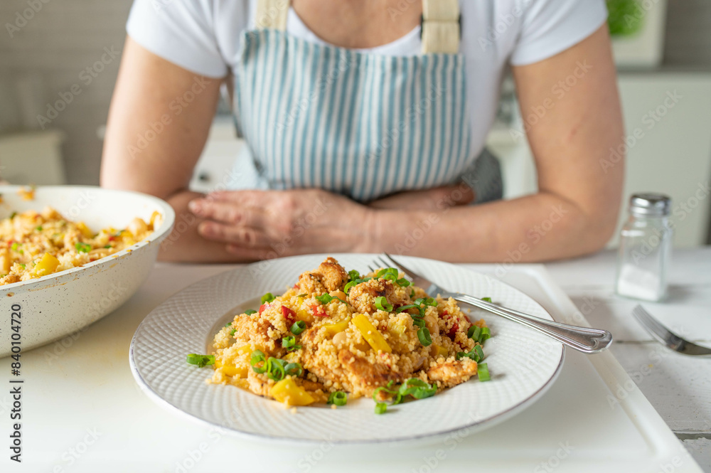 Fresh cooked healthy pan dish with couscous, chicken, beans and vegetables served by a woman with apron 