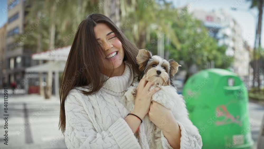 Smiling woman cuddling her terrier on a sunny city street. Smiling woman cuddling her terrier on a sunny city street.