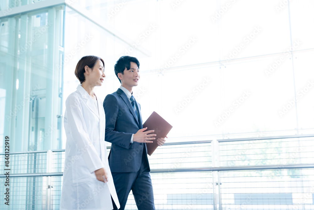 室内を歩く白衣を着た女性とスーツを着た男性 室内を歩く白衣を着た女性とスーツを着た男性