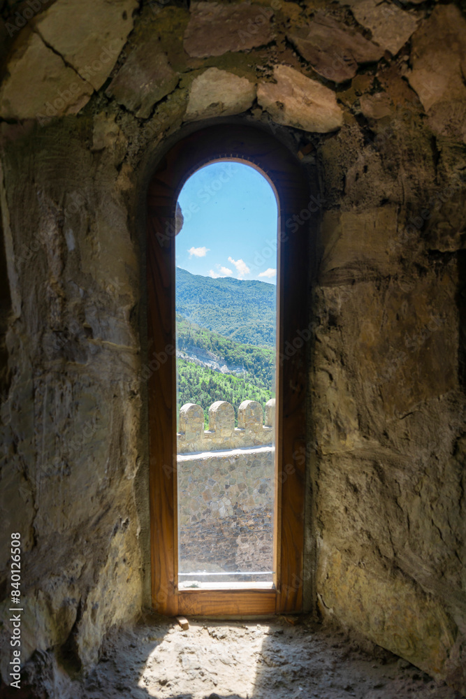 Fototapeta premium External stone wall and mountains seen through a narrow window of a church in a Dzama fortress
