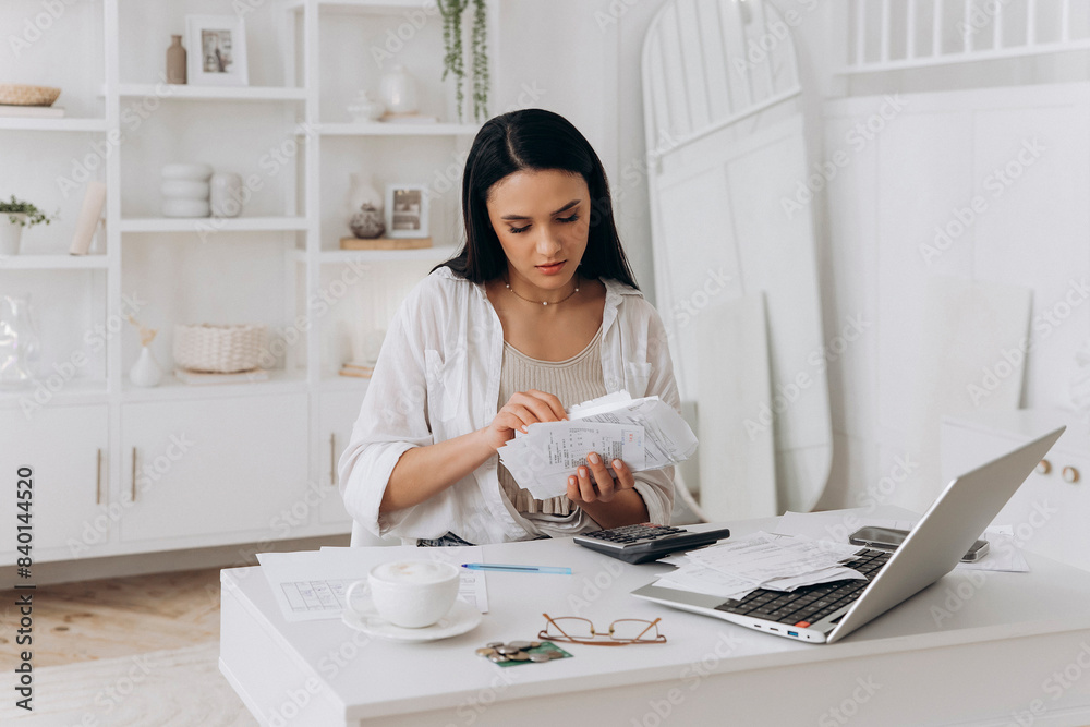 Young woman efficiently managing paperwork at desk with laptop and calculator. Reviewing documents, handling utility bills, taxes, and invoices in bright, organized home office with modern decor Young woman efficiently managing paperwork at desk with laptop and calculator. Reviewing documents, handling utility bills, taxes, and invoices in bright, organized home office with modern decor