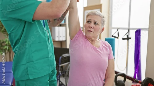 A woman patient receives physiotherapy from a male therapist in a rehabilitation clinic room. photo