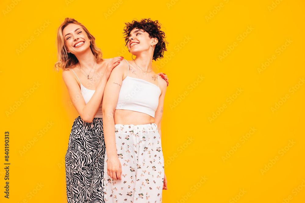 Two young beautiful smiling brunette hipster female in trendy summer clothes. Sexy women posing near yellow wall in studio. Positive models having fun. Cheerful and happy Two young beautiful smiling brunette hipster female in trendy summer clothes. Sexy women posing near yellow wall in studio. Positive models having fun. Cheerful and happy