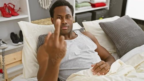 Rude awakening, young african american man in pyjamas showing a 'fuck you' gesture, a provocative expression of impoliteness right in the bedroom!
