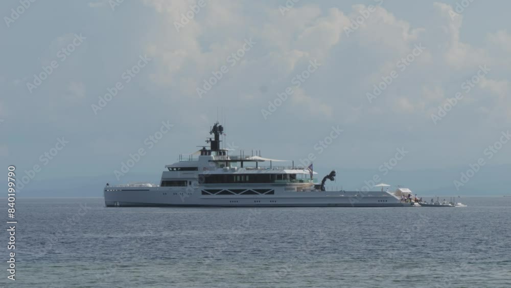 A luxurious yacht Wanderlust anchored in the calm waters. The sleek design and expansive deck space reflect opulence and relaxation, set against a backdrop of serene ocean and blue sky. Static shot. A luxurious yacht Wanderlust anchored in the calm waters. The sleek design and expansive deck space reflect opulence and relaxation, set against a backdrop of serene ocean and blue sky. Static shot.