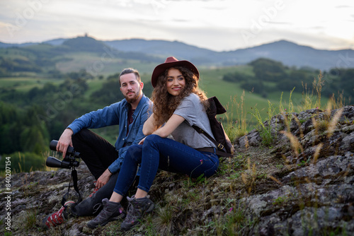 Travellers couple hiking on easy trail in nature with backpacks. Young tourist spending summer vacation oudoors, sitting on rocks and enjoying breathtaking view. © Halfpoint