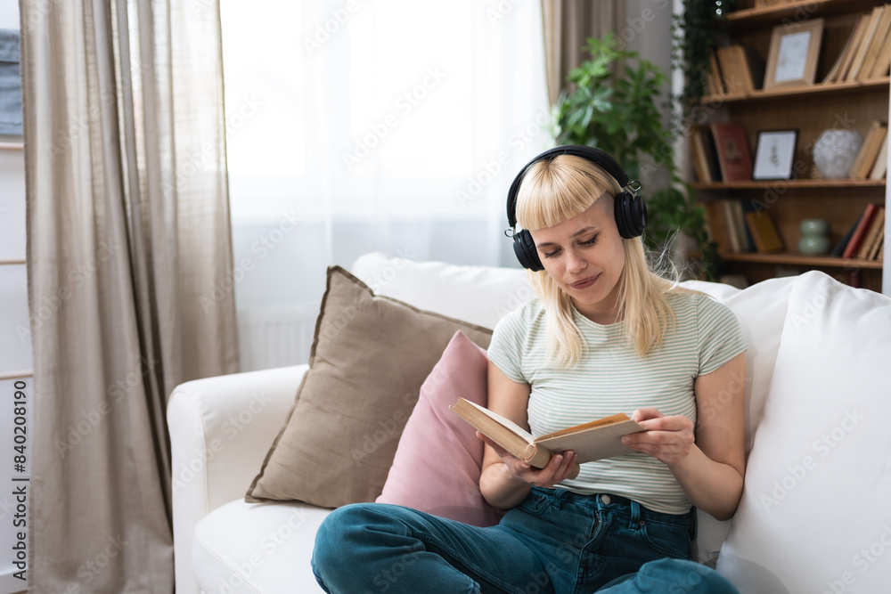Young millennial woman sitting at home on sofa listening music on wireless headphones read book enjoy life and freedom. Educated university student girl resting and relaxing with mix tape and reading. Young millennial woman sitting at home on sofa listening music on wireless headphones read book enjoy life and freedom. Educated university student girl resting and relaxing with mix tape and reading.