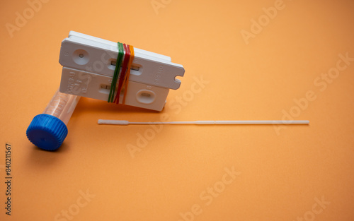 A few of Covid-19 rapid antigen test casettes tied with rubber bands, with a nasal swab and test tube; isolated on orange background. A close-up and selective focus photo of the test cassette.  photo